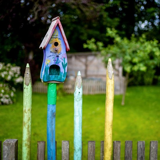 Zaun mit bunten Ästen und bunt bemaltem Vogelhaus